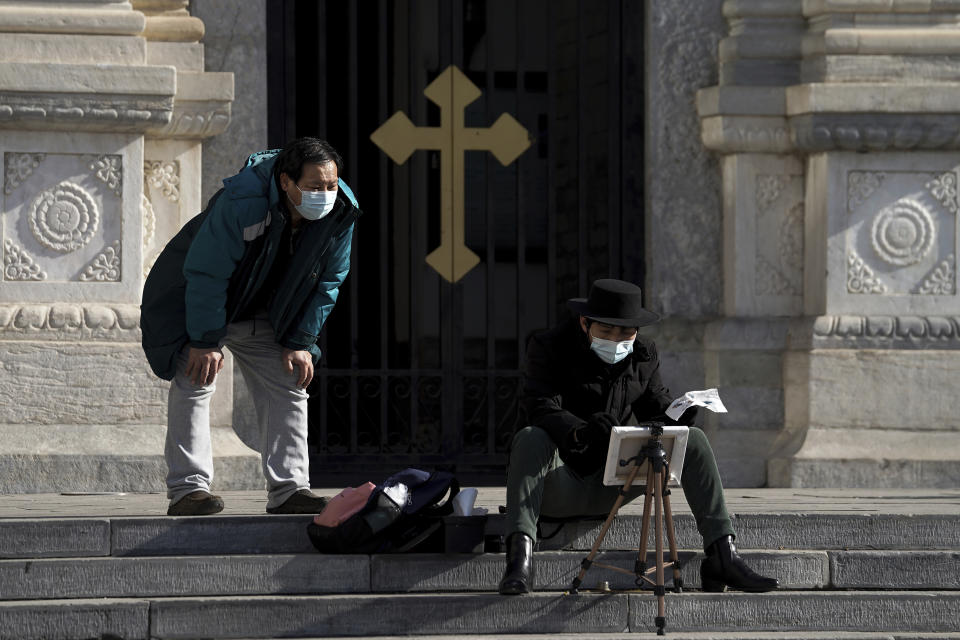 A man wearing a face mask to help curb the spread of the coronavirus looks at a masked man drawing outside a church in Beijing, Monday, Jan. 18, 2021. A Chinese province grappling with a spike in coronavirus cases is reinstating tight restrictions on weddings, funerals and other family gatherings, threatening violators with criminal charges. (AP Photo/Andy Wong)