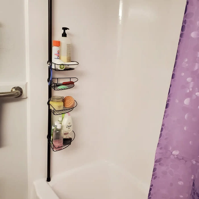 Reviewer's photo of the tension pole shower organizer in the color bronze, holding various bath products next to a purple shower curtain