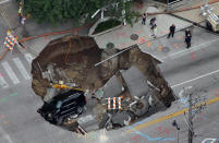 A Cadillac Escalade sits at the bottom of a sinkhole in Milwaukee, Wis. on Friday, July 23, 2010, still running almost 20 hours after the driver fell in. On Thursday, powerful storms pounded southeastern Wisconsin and caused widespread flooding. (AP Photo/Mark Was)