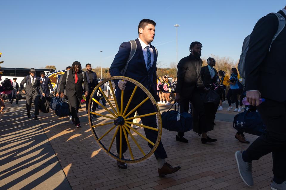 Kent State grad student center Sam Allan carries the Wagon Wheel into Dix Stadium as the team arrives for today's game against the Akron Zips.