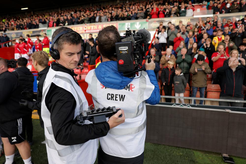 The documentary crew film the crowd as the teams come out for kick off.