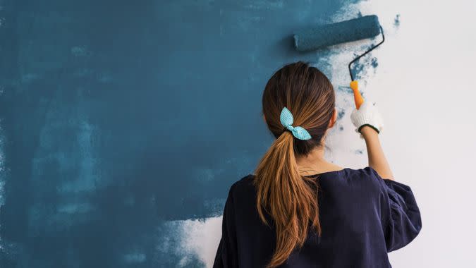 Young asian happy woman painting interior wall with paint roller in new house.