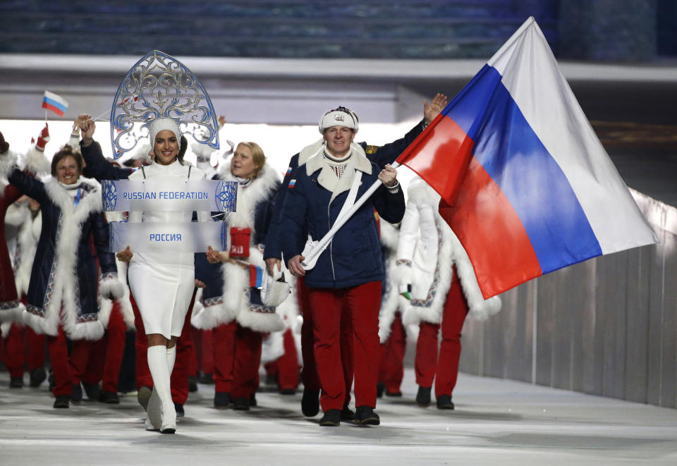 FILE - Bobsledder Alexander Zubkov carries the Russian flag next to model Irina Shayk holding the country’s identification sign at the opening ceremony of the 2014 Winter Olympics in Sochi, Russia, on Feb. 7, 2014. The Sochi Olympics were a pet project of President Vladimir Putin as he sought to project Russia’s global clout, boost its prestige and impress the world. But the Kremlin’s attempt at soft power soon collided with hard realities. (AP Photo/Mark Humphrey, File)