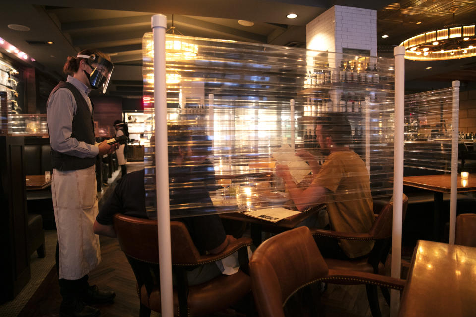 FILE - In this June 22, 2020, file photo, wearing a face shield, server Brandon Fricke, left, takes orders from dine-in customers surrounded by protective dividers at Water Grill seafood restaurant in Los Angeles. Restaurants and stores have been forced to make changes to survive. (AP Photo/Jae C. Hong, File)