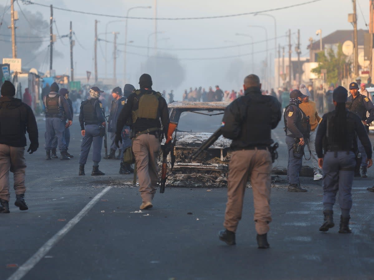 Cape Town law enforcement officials stand around a burnt-out vehicle in Nyanga (REUTERS/Esa Alexander)