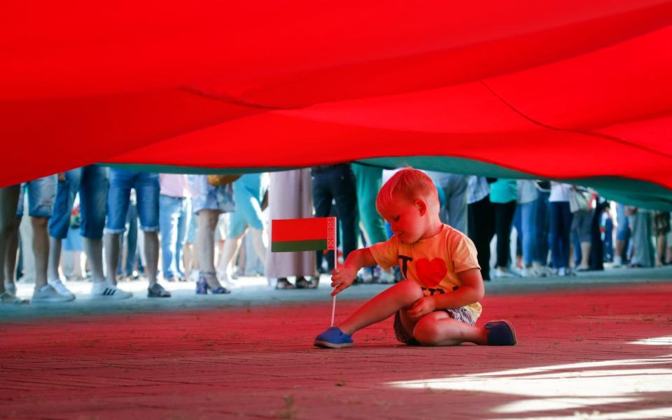 A boy plays sitting under a huge Belarusian State flag during a pro-government rally of Belarusian President Alexander Lukashenko's supporters in the Brest Fortress memorial, in Brest - AP