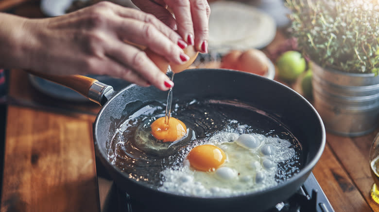 person cracking egg into skillet
