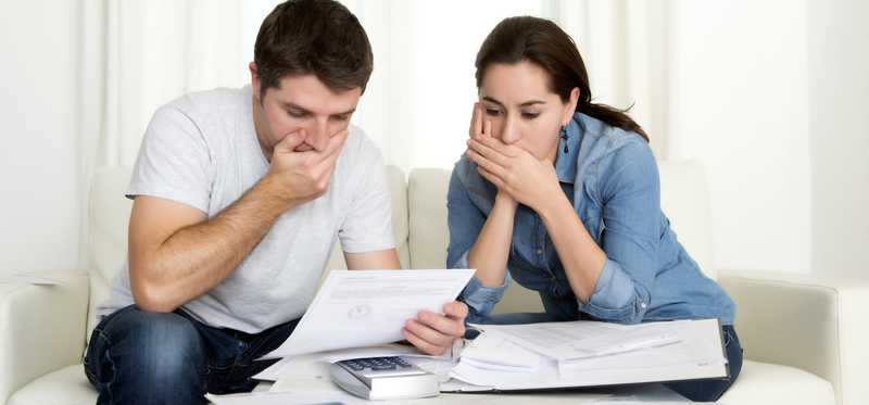 Couple looking at bills with hands over their mouths.