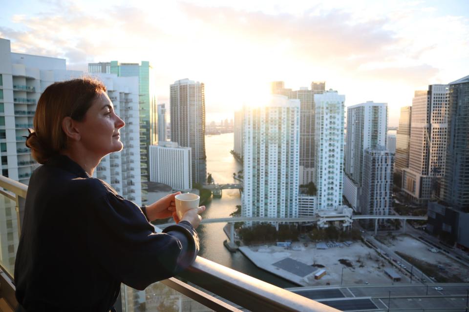 Woman enjoying cup of coffee while looking at Miami, Florida skyline from a balcony.