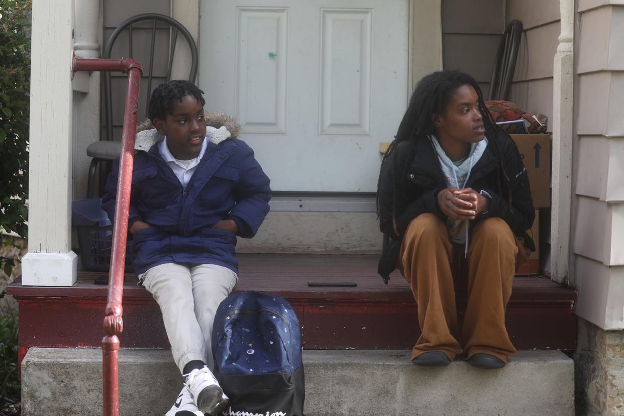 Adrian Burrows, 10, a fifth grader at School 52, waits for the bus with his mother, Adriana Jackson in front of their home. Both spy the bus coming down Grand Avenue. The bus is often late, making him also late to school.