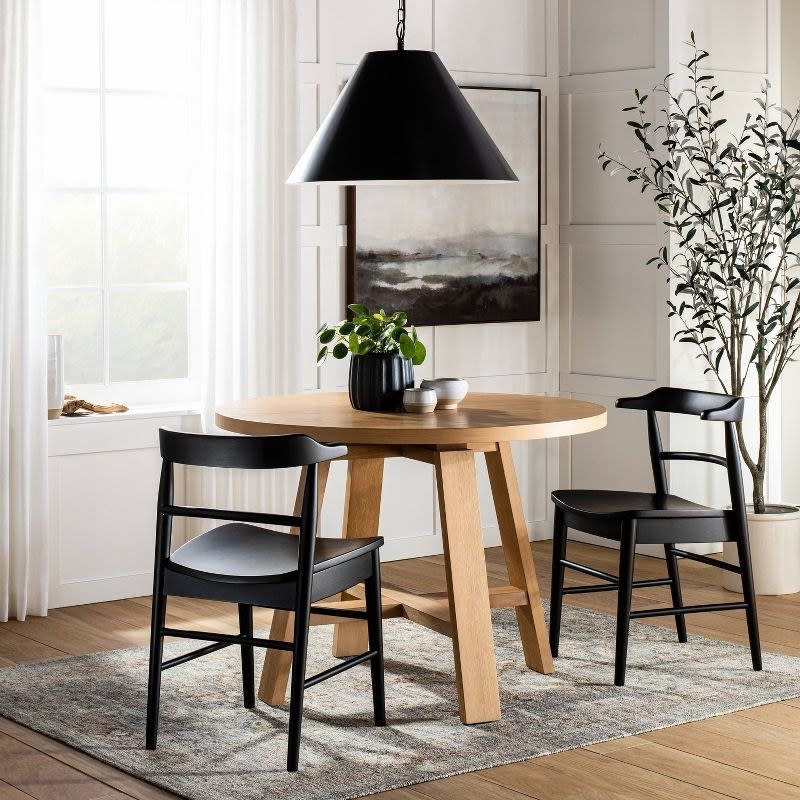 Round wooden dining table with modern black chairs in a well-lit room with decor. Perfect for home dining spaces