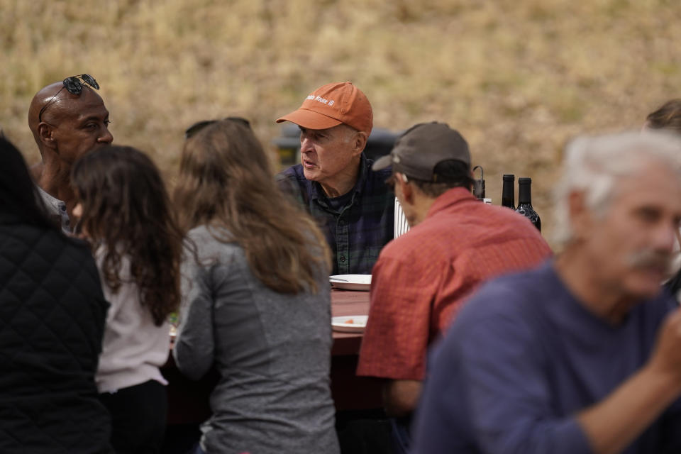 Former California Gov. Jerry Brown, center in orange hat, has lunch with friends and old colleagues who traveled to Colusa County ranch to help him with the olive harvest on his ranch near Williams, Calif., Saturday, Oct. 30, 2021. Brown is living off the grid in retirement, but he's still deeply connected on two issues that captivated him while in office and now are center stage globally: climate change and the threat of nuclear war. (AP Photo/Rich Pedroncelli)