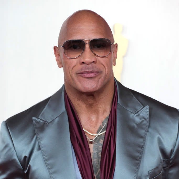 Dwayne Johnson in a shiny suit with a satin burgundy scarf, smiling