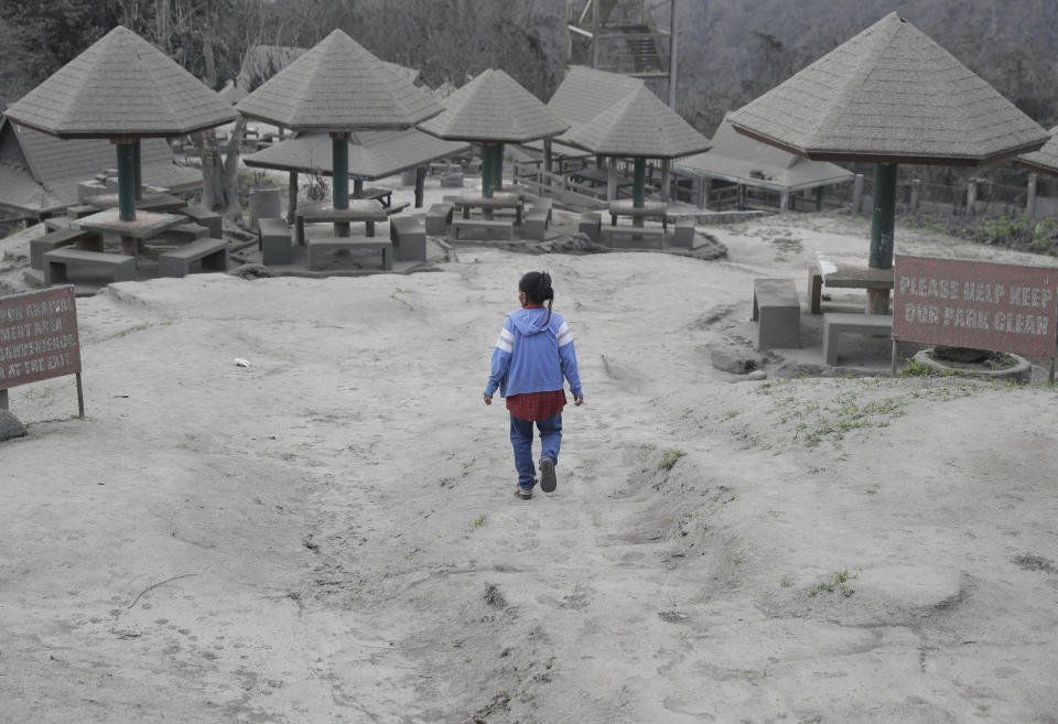 A woman walks along a park covered in volcanic-ash at a town near Taal volcano in Tagaytay, Cavite province, southern Philippines on Sunday Jan. 19, 2020. Philippine officials said Sunday the government will no longer allow villagers to return to a crater-studded island where an erupting Taal volcano lies, warning that living there would be "like having a gun pointed at you." (AP Photo/Aaron Favila)