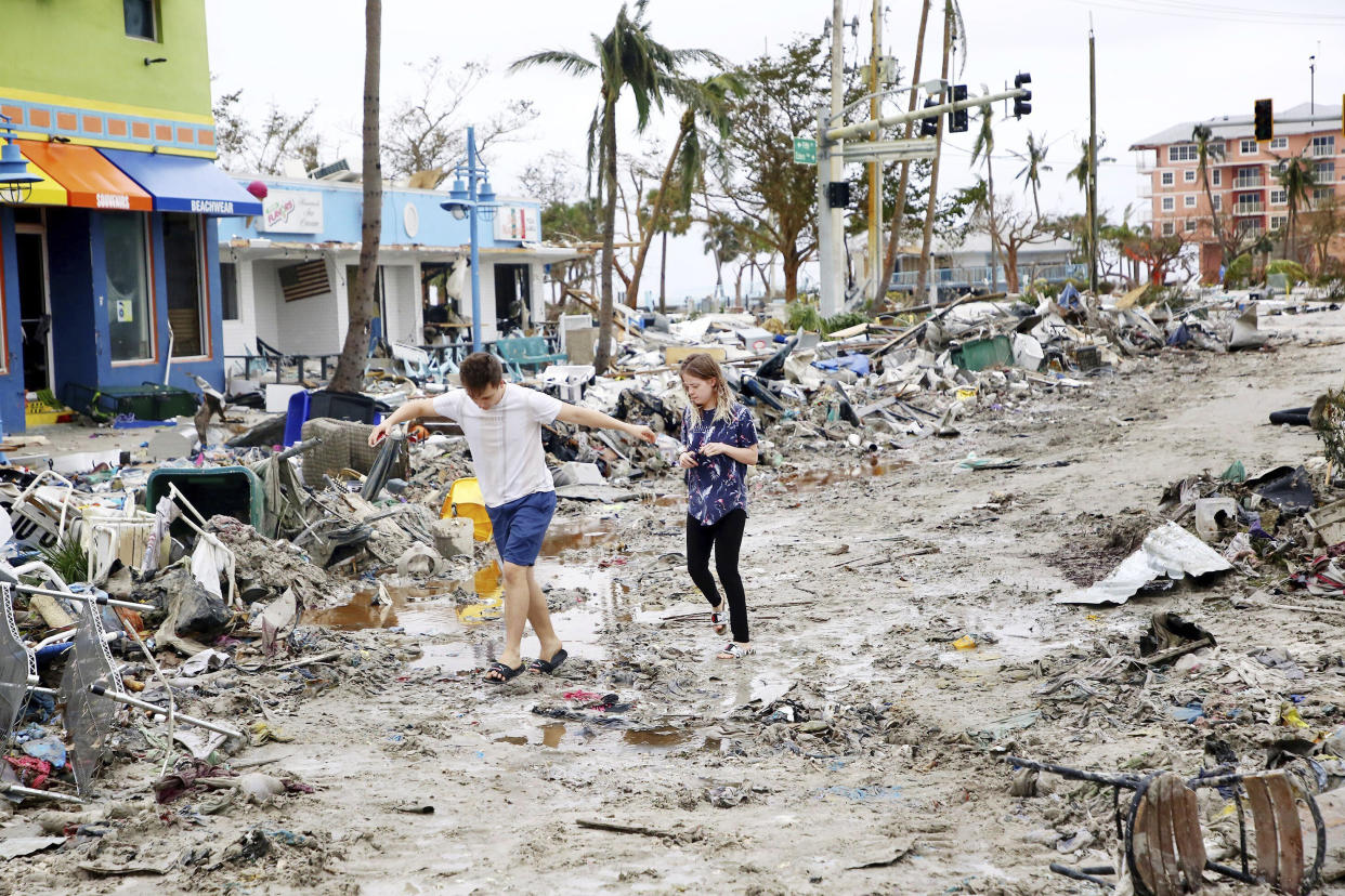 Jake Moses and Heather Jones walk through debris along a street with destroyed businesses.