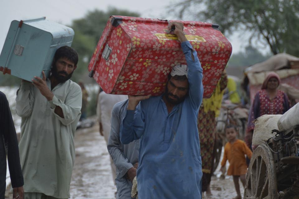 Displaced people carry belongings after they salvaged usable items from their flood-hit home as they wade through a flooded area in Jaffarabad, a district of Pakistan's southwestern Baluchistan province, Thursday, Aug. 25, 2022. Pakistan's government in an overnight appeal sought relief assistance from the international community for flood-affected people in this impoverished Islamic nation, as the exceptionally heavier monsoon rain in recent decades continued lashing various parts of the country. (AP Photo/Zahid Hussain)