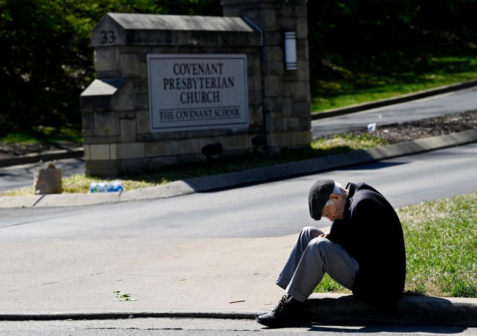 A man sits on the curb near a makeshift memorial by the entrance of the Covenant School on Wednesday in Nashville, Tenn.