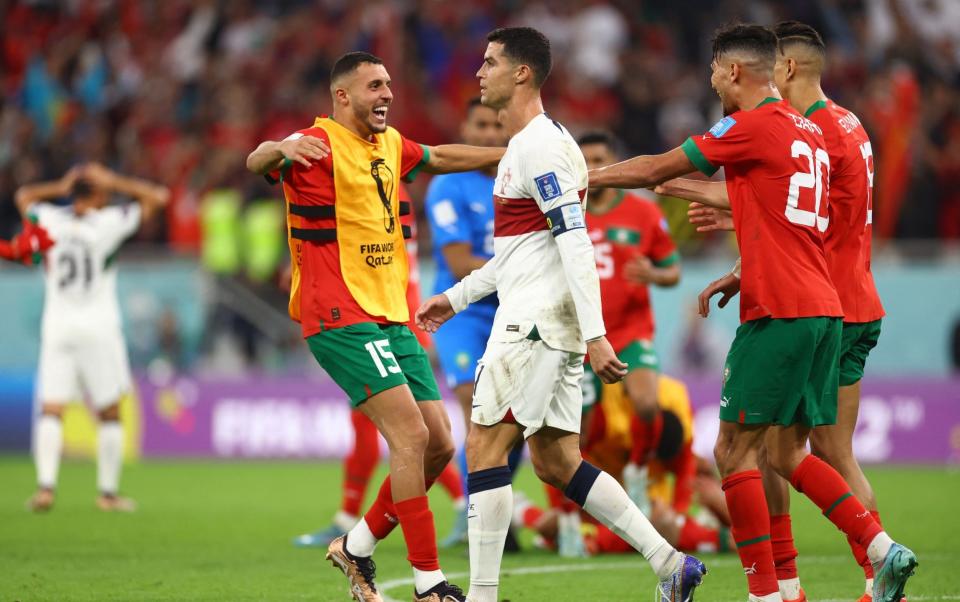 Portugal's Cristiano Ronaldo looks dejected after being eliminated from the World Cup as Morocco players celebrate qualifying - REUTERS