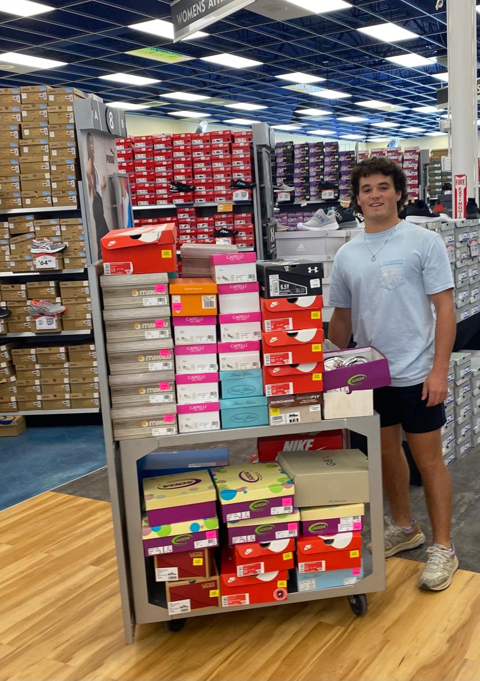 Gunner Robinson poses in front of a cart of shoes he purchased with donations from his chairty Gunner's Runners.