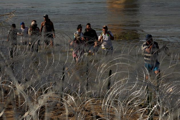 Migrants walk in the Rio Grande along a wall of concertina wire as they try to cross into the U.S. from Mexico on Friday in Eagle Pass, Texas.