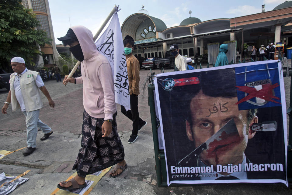 Muslim men walk past a defaced poster of French President Emmanuel Macron during a protest at Al Jihad mosque in Medan, North Sumatra, Indonesia, Friday, Oct. 30, 2020. Muslims around the world have been calling for both protests and a boycott of French goods in response to France's stance on caricatures of Islam's most revered prophet. (AP Photo/Binsar Bakkara)