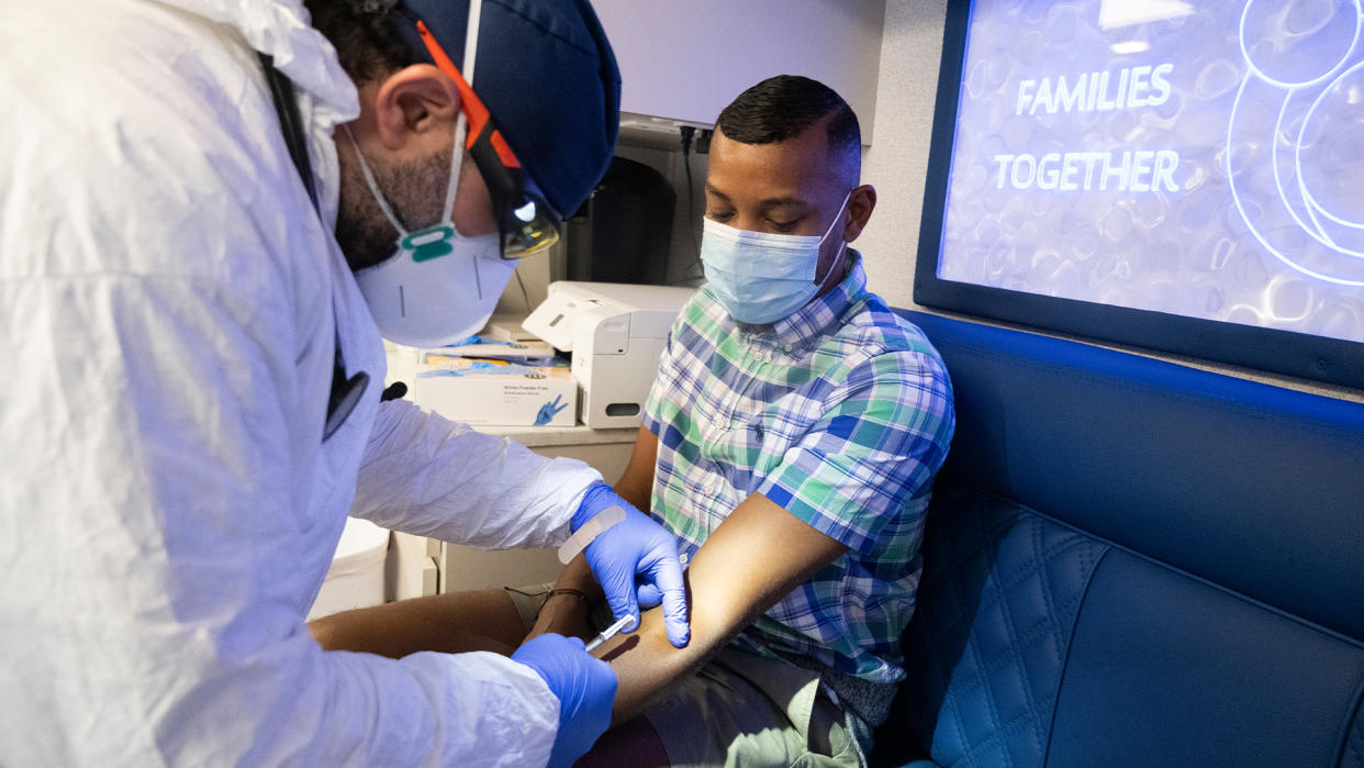  Health care worker in an n95 mask prepares to give a vaccine into the forearm of a young man wearing a surgical mask. 