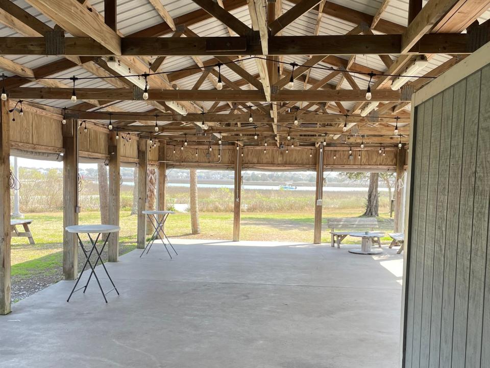 Wooden pavilion with intricate wooden beams and a sage-green wall in foreground and woods in the background