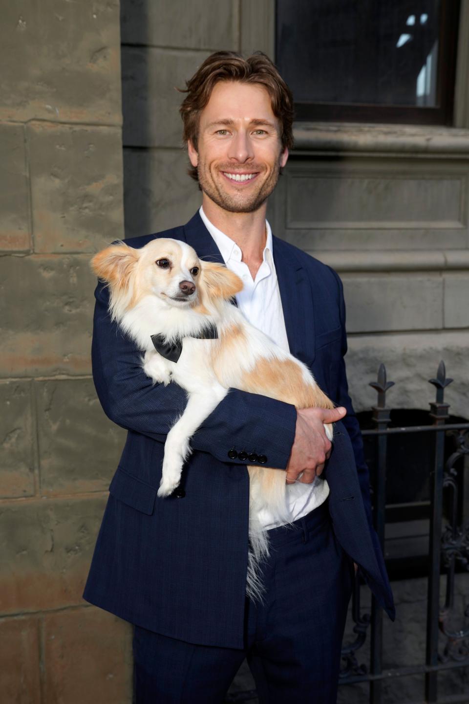 Man in a suit, holding a small dog, smiles at the camera