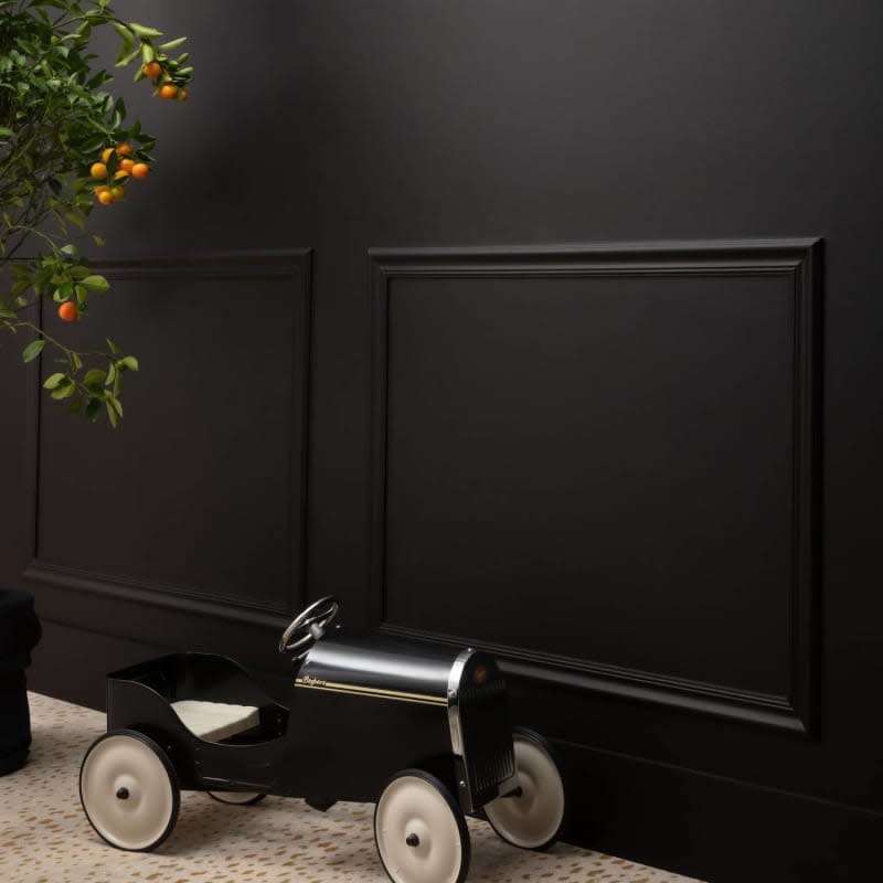 Dark black matte paint on walls with wainscoating and small black toy car with orange fruit tree