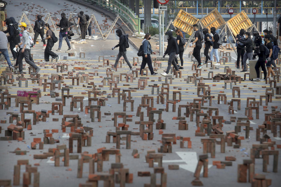 Protesters walk past barricades of bricks on a road near the Hong Kong Polytechnic University in Hong Kong, Thursday, Nov. 14, 2019. Hong Kong residents endured a fourth day of traffic snarls and mass transit disruptions Thursday as protesters closed some main roads and rail networks while police skirmished with militant students at major universities. (AP Photo/Kin Cheung)