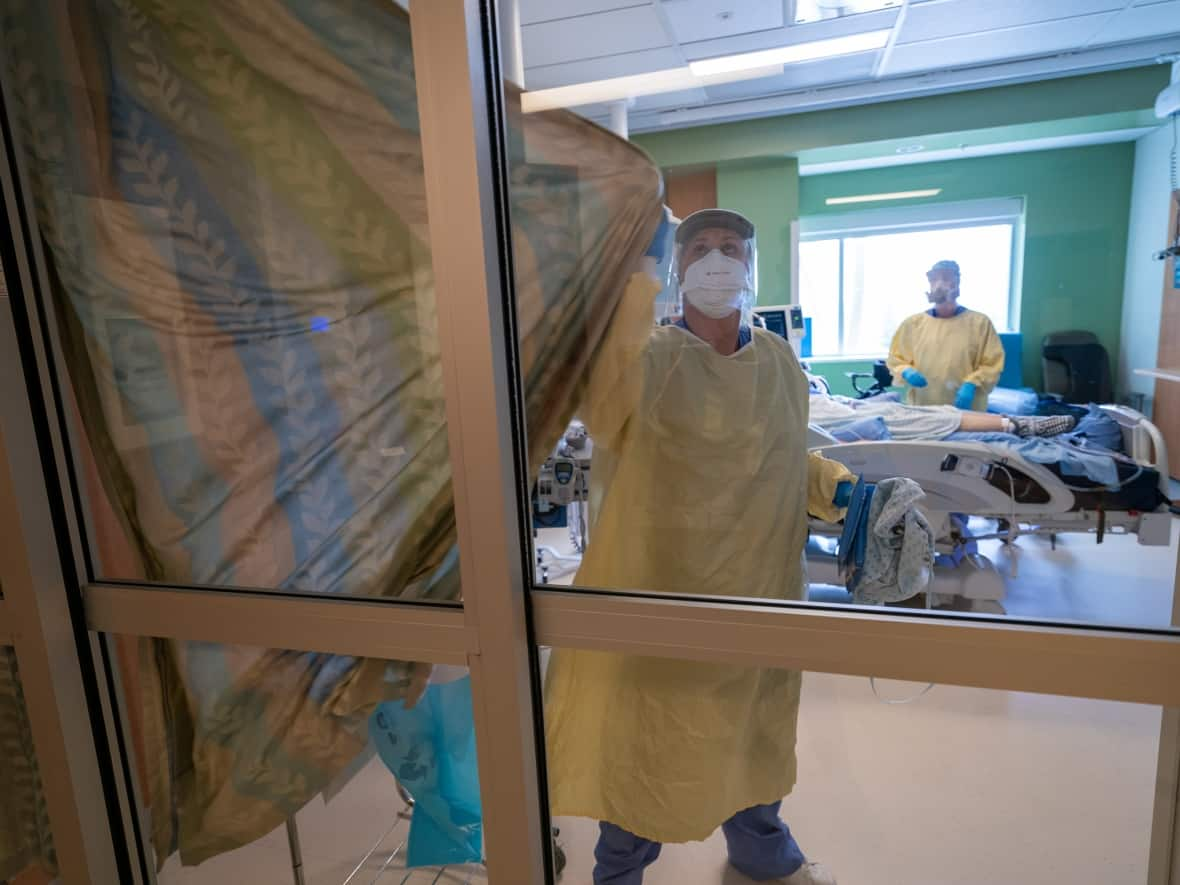 Nurses close the curtains of a patient's room in the COVID-19 intensive care unit at Surrey Memorial Hospital in Surrey, B.C., in June 2021. The stresses of COVID-19 hospitalizations, driven by the current wave of infections, are being felt acutely across the country. (Jonathan Hayward/The Canadian Press - image credit)