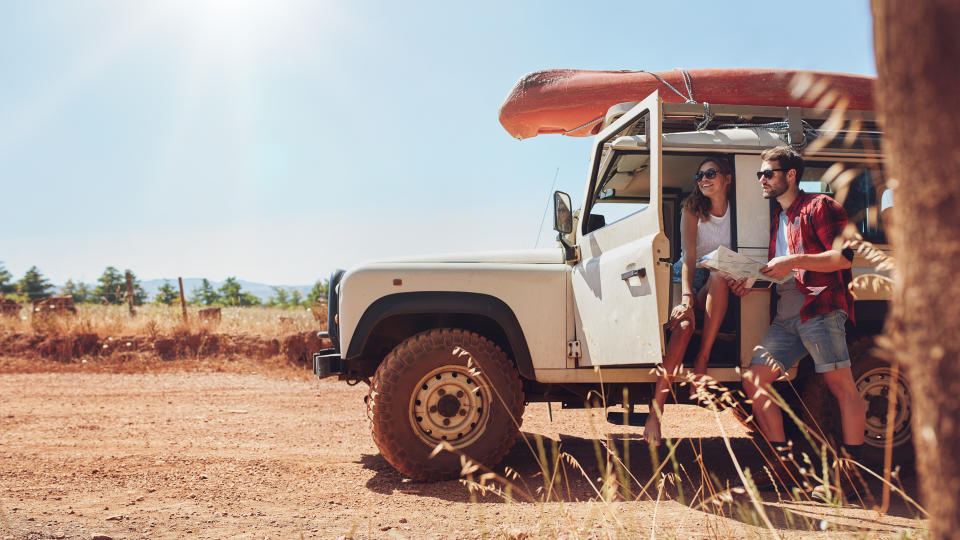 Young couple with car on road trip reading map for directions.