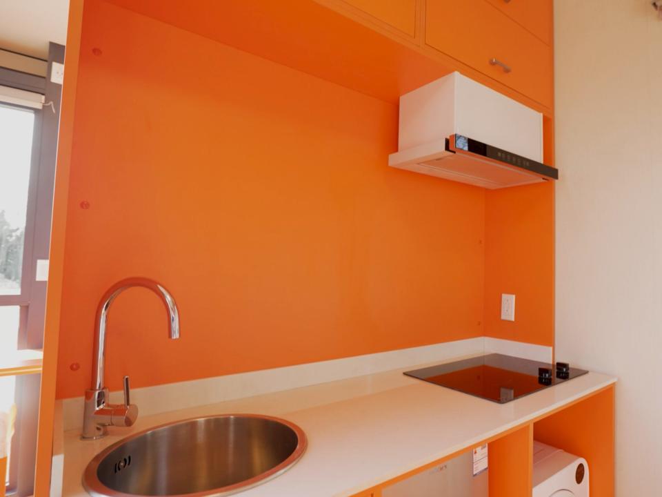 The kitchen inside Nestron's tiny home with an orange wall and amenities like a sink