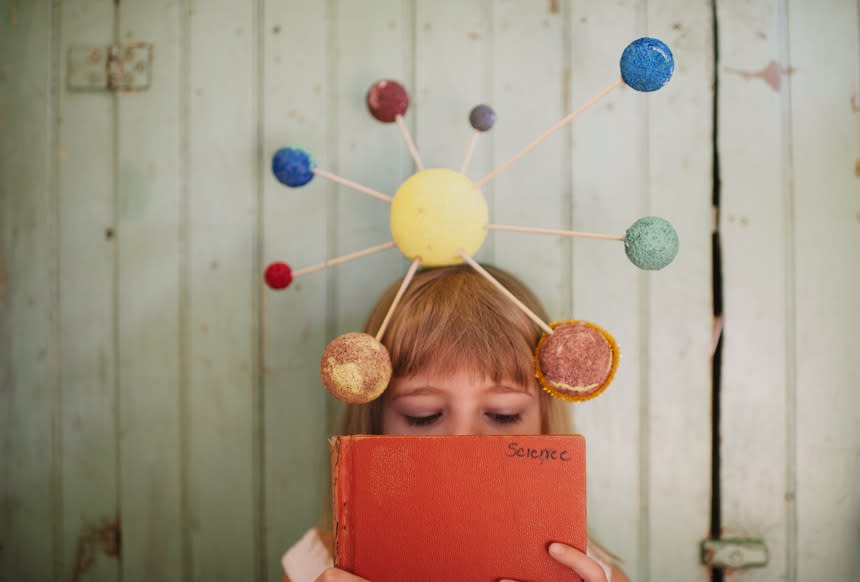 Young girl reads a science text book wearing a solar system model headpiece.