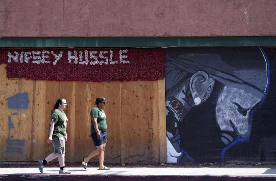 Pedestrians walk past a mural of the late rapper Nipsey Hussle, Thursday, June 30, 2022, near the location of his closed The Marathon Clothing store in Los Angeles. The many murals of Hussle around Los Angeles speak to the late rapper's lasting legacy.(AP Photo/Chris Pizzello)