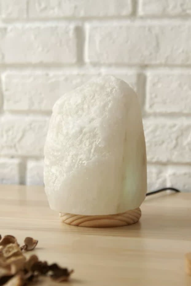 Himalayan salt lamp on a wooden base placed on a table with a white brick wall background