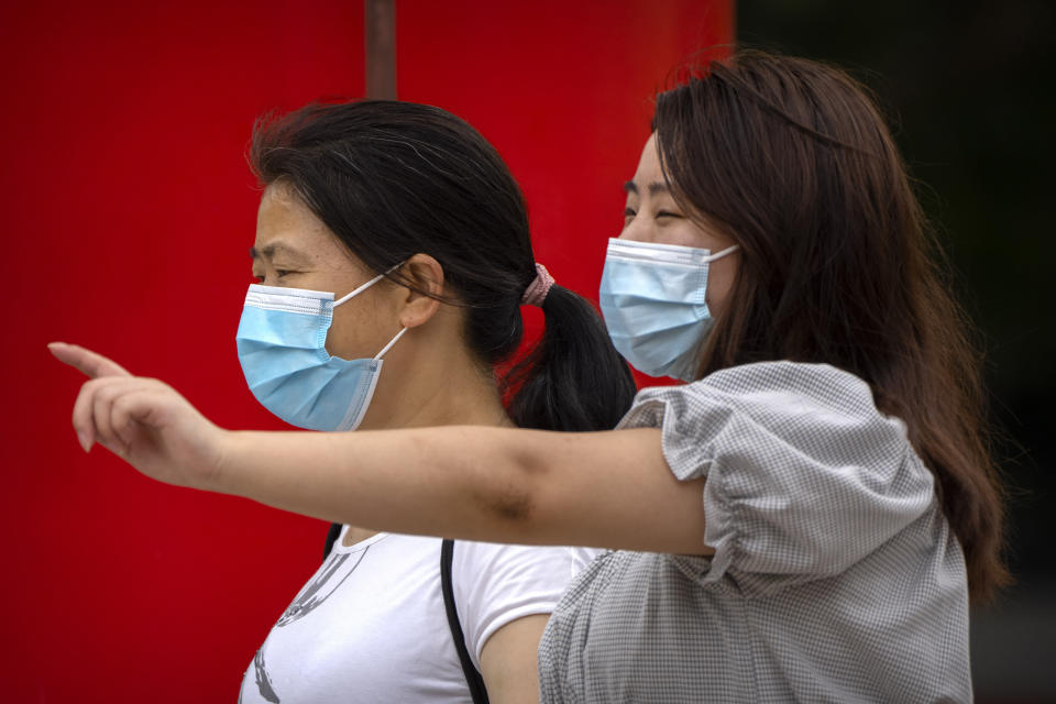 Women wearing face masks walk at a public park in Beijing, Tuesday, June 28, 2022. (AP Photo/Mark Schiefelbein)