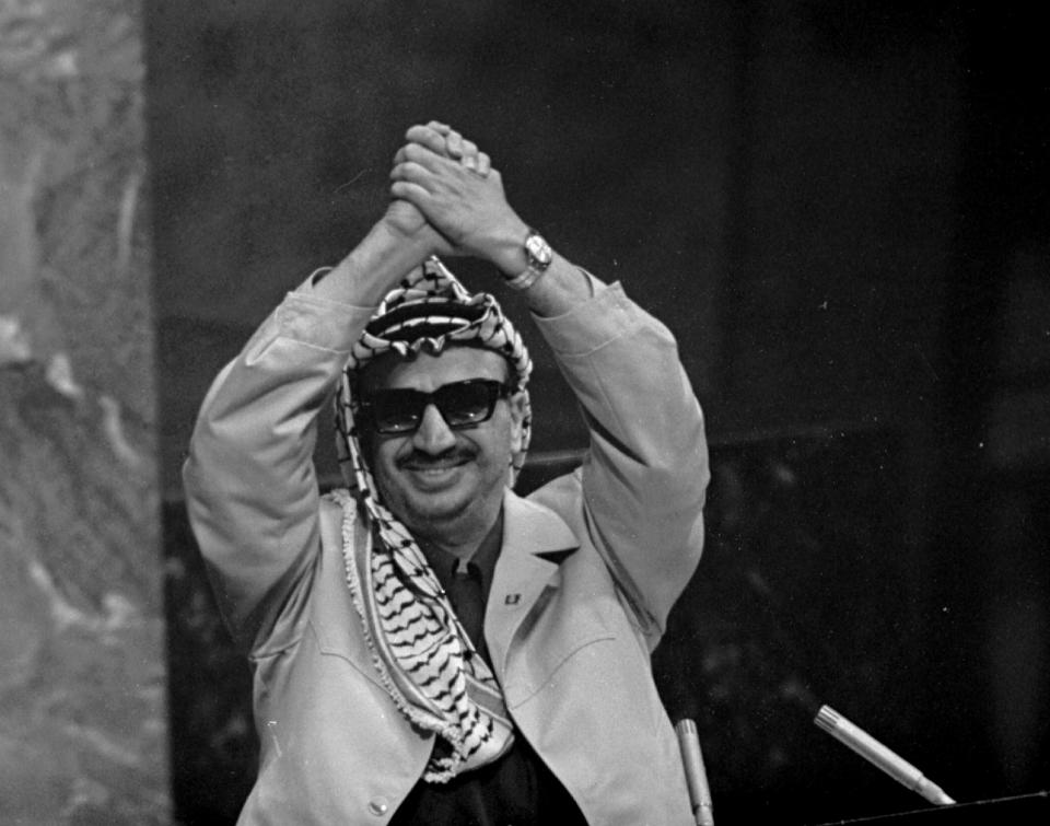 FILE - In this Nov. 13, 1974 file photo, Yasser Arafat clasps his arms over his head as he addresses the United Nations General Assembly, at U.N. headquarters. In 1974, Arafat was invited to represent the Palestine Liberation Organization and his people before the world body, where he made it clear he was ready to use any means for statehood. He spoke of oppressed people and liberation the world over. Wearing his trademark Palestinian keffiyeh scarf, he concluded with an enduring quote: "Today I have come bearing an olive branch and a freedom fighter's gun. Do not let the olive branch from my hand." (AP Photo/Marty Lederhandler, File)