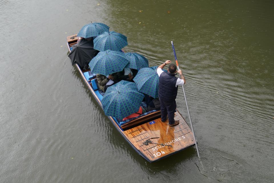 People shelter from the rain under umbrellas as they punt along the River Cam in Cambridge. (PA)