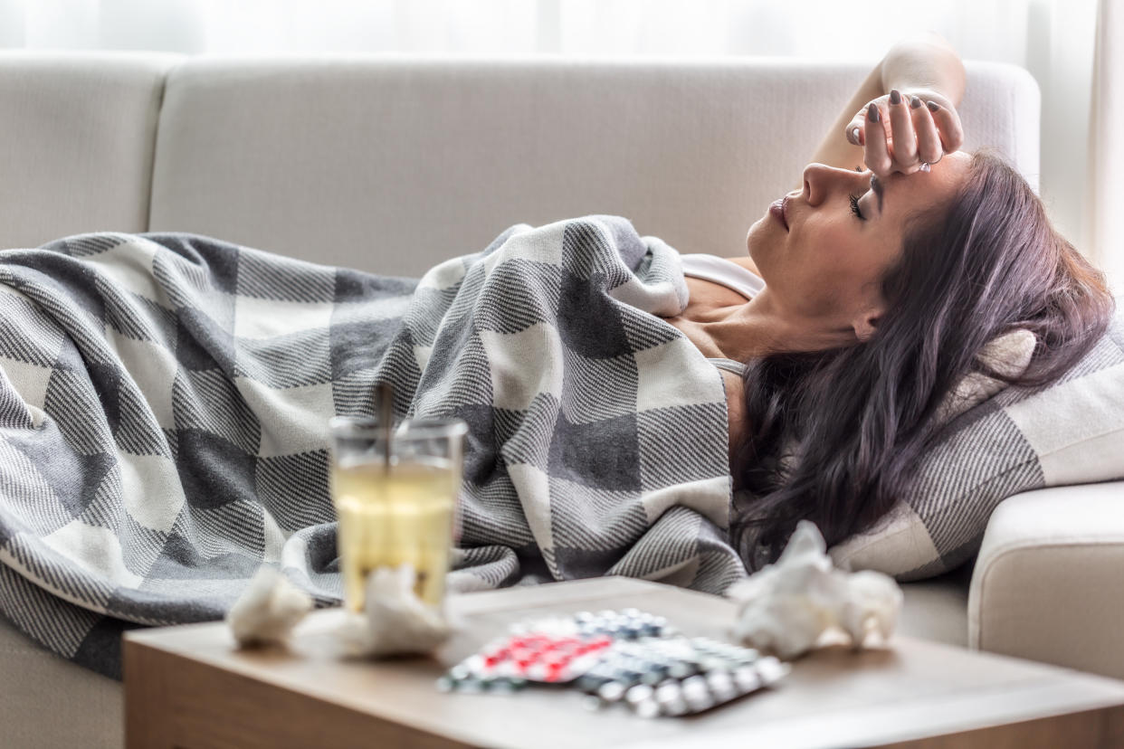 Woman having symptoms of Covid-19 lies covered in blanket in isolation with handerchiefs and pills next to her.