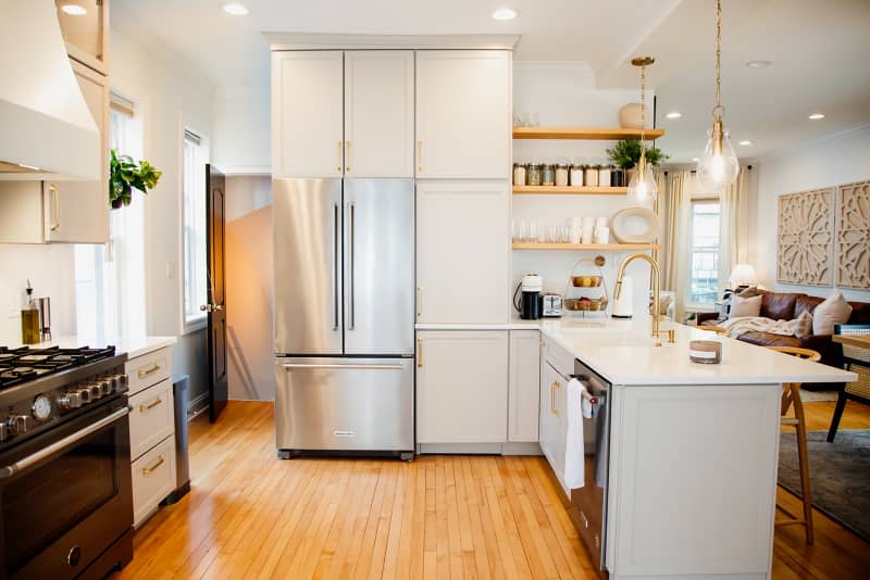 Neutral colored cabinets with brass hardware in open kitchen with open shelving and two large bulb pendant lights over countertop.