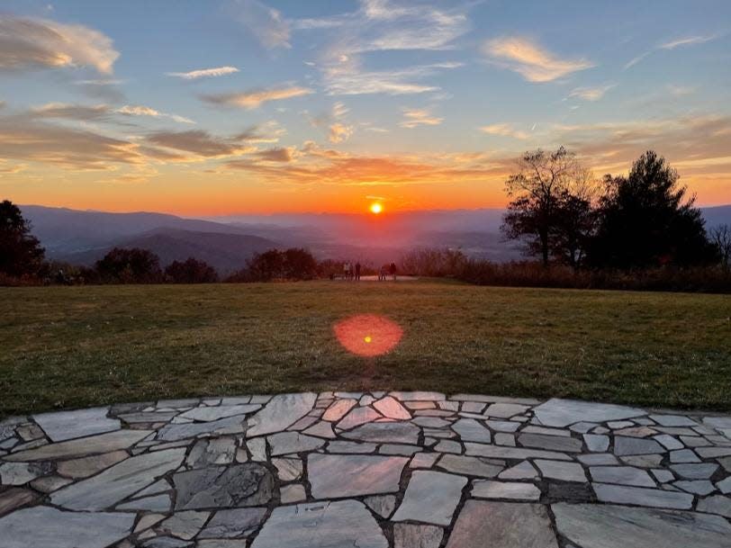 The sunset at Dickey Ridge Visitor Center at Shenandoah National Park. There is a path of flat stones, a large field of grass, and trees and mountains in the distance.