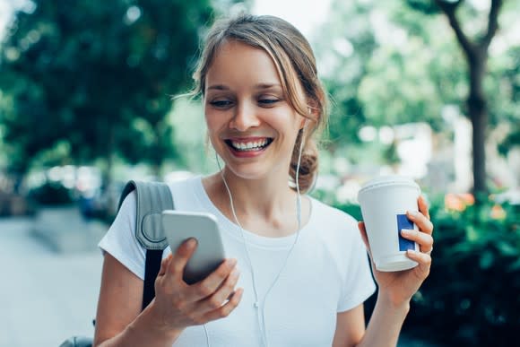 A young woman looks at her smartphone as she drinks coffee.