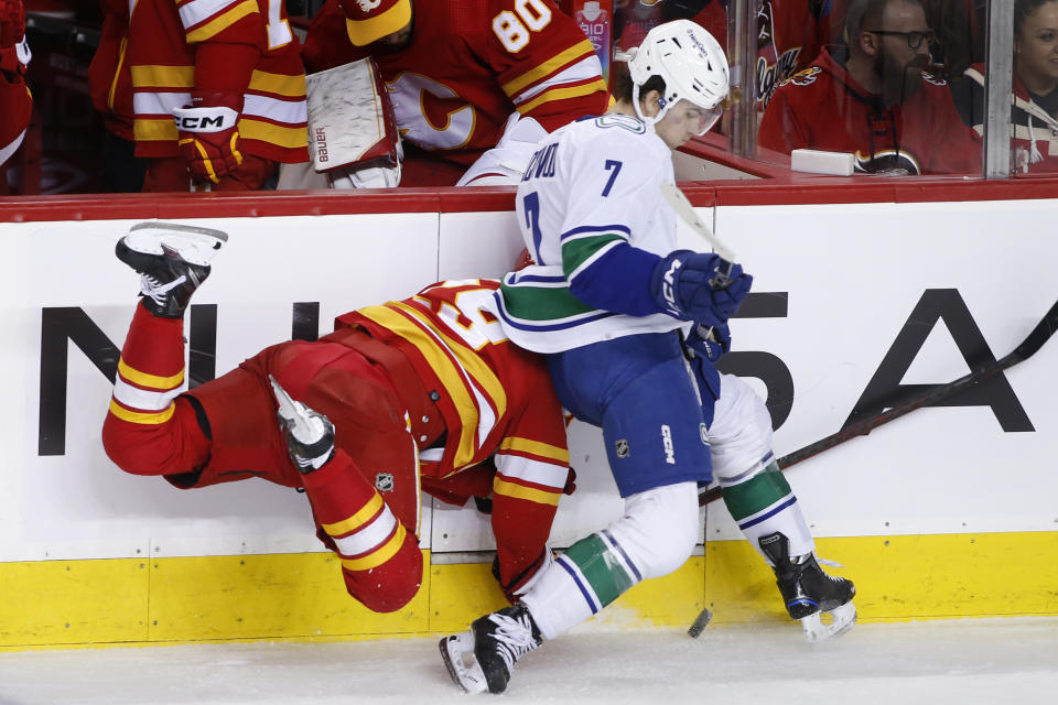 Calgary Flames' Dillon Dube, left, is knocked off the puck and sent headfirst into the boards by Vancouver Canucks' William Lockwood during the second period of an NHL hockey game Saturday, Dec. 31, 2022, in Calgary, Alberta. (Larry MacDougal/The Canadian Press via AP)