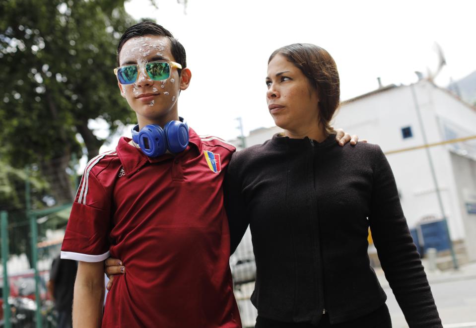16-year-old Rufo Chacon, wearing reflective sunglasses, and his mother Adriana Parada are met by a gaggle of reporters as they arrive to the offices of Foro Penal, a Venezuelan human rights organization, in Caracas, Venezuela, Friday, July 19, 2019. A Venezuelan teenager who lost his eyesight when he was hit by police buckshot during a protest says he wants to continue studying. (AP Photo/Ariana Cubillos)