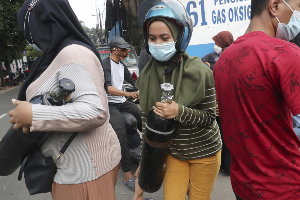 A woman carries her oxygen tank after having it refilled at a recharging station in Jakarta, Indonesia, Friday, July 9, 2021. The world's fourth most populous country is running out of oxygen as it endures a devastating wave of coronavirus cases and the government is seeking emergency supplies from other countries, including Singapore and China. (AP Photo/Tatan Syuflana)