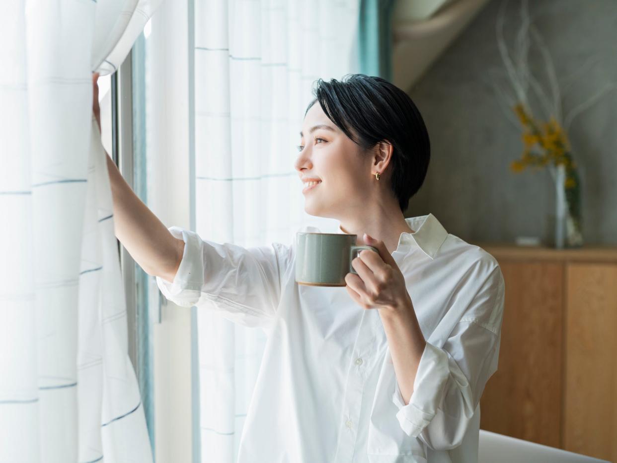 A person enjoying early morning coffee, looking out the window in a brightly-lit office