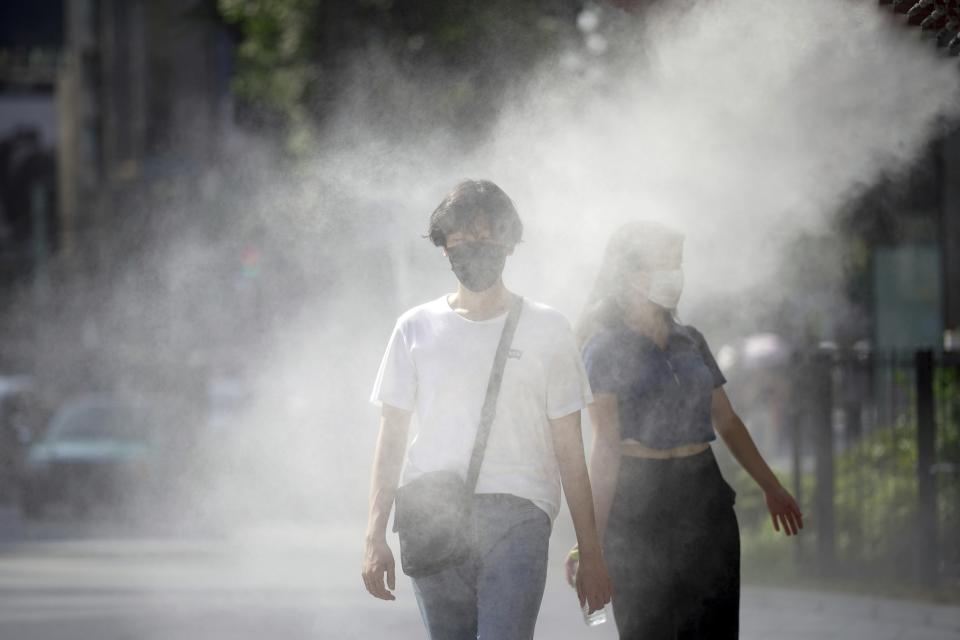 FILE - People wearing face masks to help protect against the spread of the coronavirus cool off at a cooling mist spot Aug. 1, 2022, in Tokyo. Temperatures are rising in Japan and summer is coming fast. (AP Photo/Eugene Hoshiko, File)
