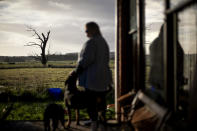 With her favorite tree in the background, Carmall Casey stands for a photo on her front porch in Black River, Tasmania, Australia, Wednesday, July 24, 2019. The tree is dead and gnarled, but still standing. Like her, she says, it's old and broken, but still good for something. "But dead trees, even though they're dead, they've still got beauty of some kind haven't they?" (AP Photo/David Goldman)