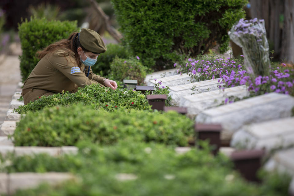 An Israeli soldier wearing a protective face mask amid concerns over the country's coronavirus outbreak, lights candles next to graves of fallen soldiers on the eve of memorial Day in Kiryat Shaul Military Cemetery in Tel Aviv, Israel, Monday, April 27, 2020. This year the government had banned public memorial services at military cemeteries as part of its measures to help stop the spread of the virus. Israel marks the annual Memorial Day in remembrance of soldiers who died in the nation's conflicts, beginning at dusk Monday until Tuesday evening. (AP Photo/Oded Balilty)